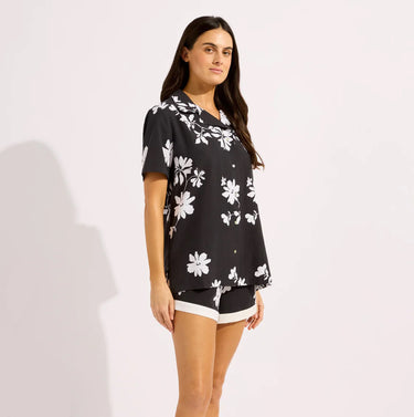 A woman wearing a button up Hawaiian flower shirt and short set