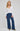 Woman wearing a white sweater and blue jeans on a plain background
