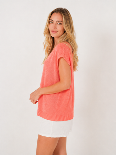 Woman wearing a coral sweater over a white shirt on a plain background
