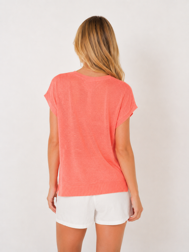 Woman wearing a coral sweater and white shorts on a plain background