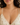 A close-up of a woman wearing a delicate gold Y-necklace with small blue and dark gray stones, paired with a cream floral camisole.