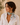 A woman wearing a white cotton neck scarf with a colorful botanical print and gold jewelry, styled with a white linen shirt against a warm beige background.